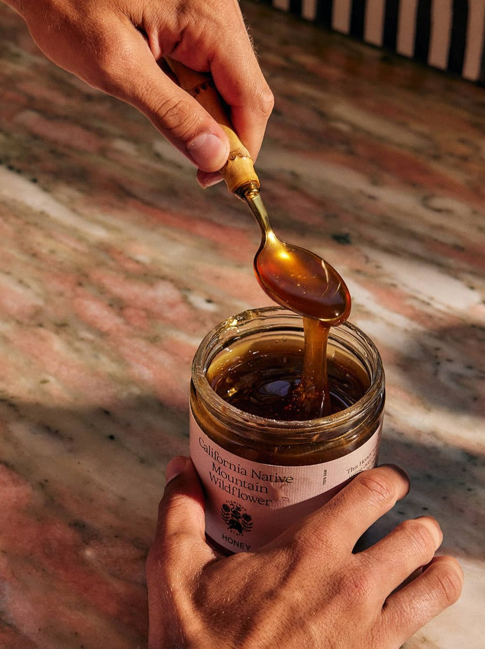Hand Holding Gold Spoon Dripping Honey Into An Open Jar
