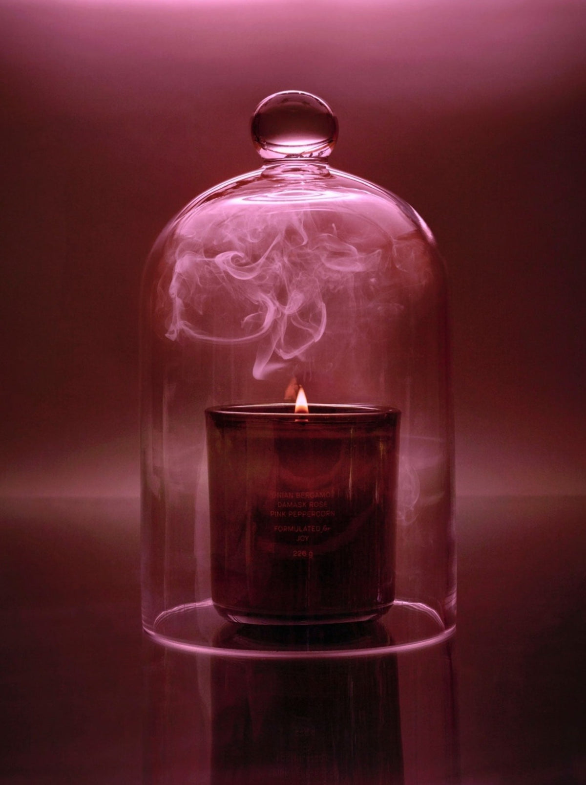 A lit candle emits smoke inside a glass cloche.