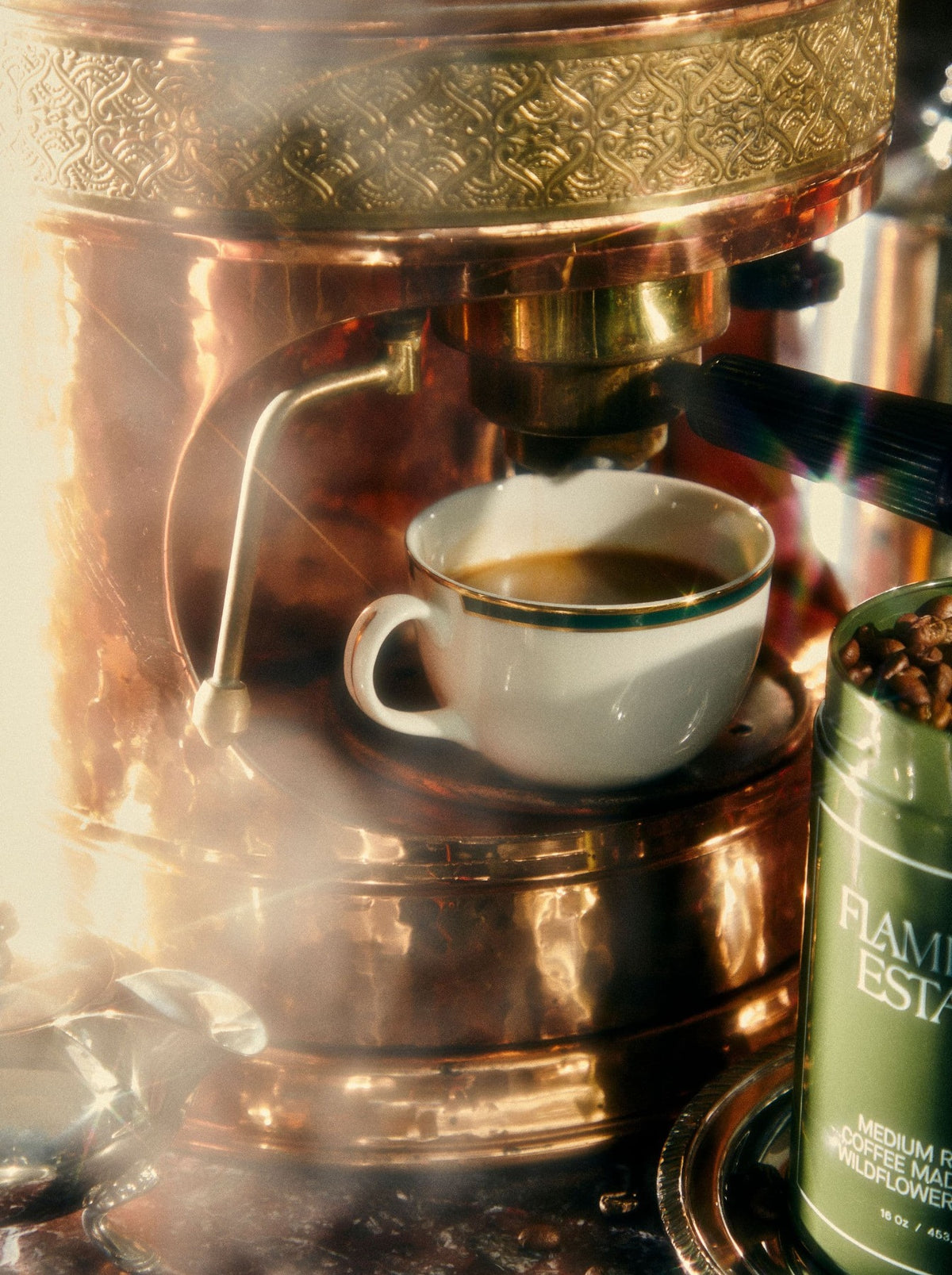 A white cup receives espresso from a vintage copper coffee machine.
