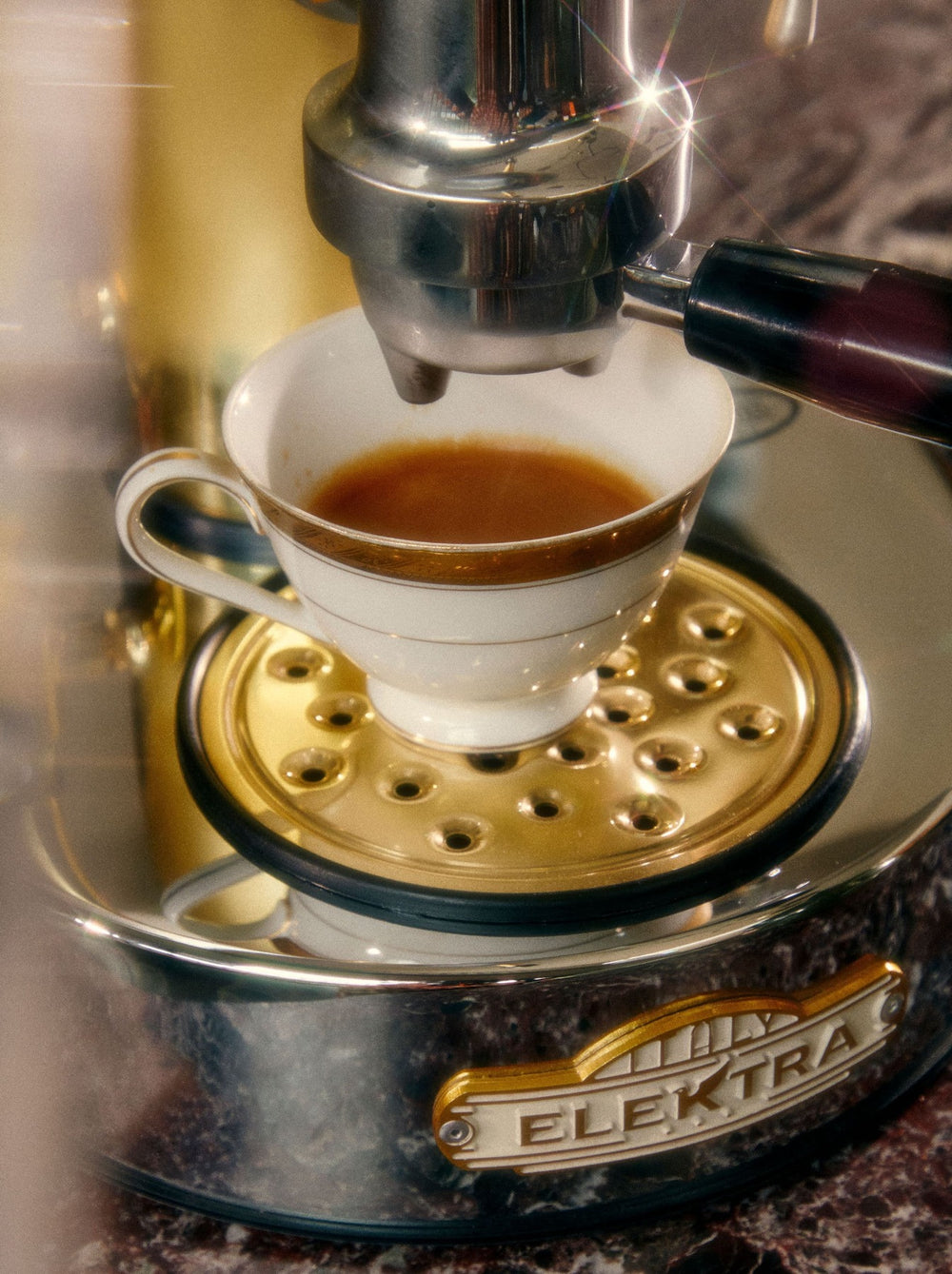 A white cup catches espresso flowing from a shiny chrome espresso machine.