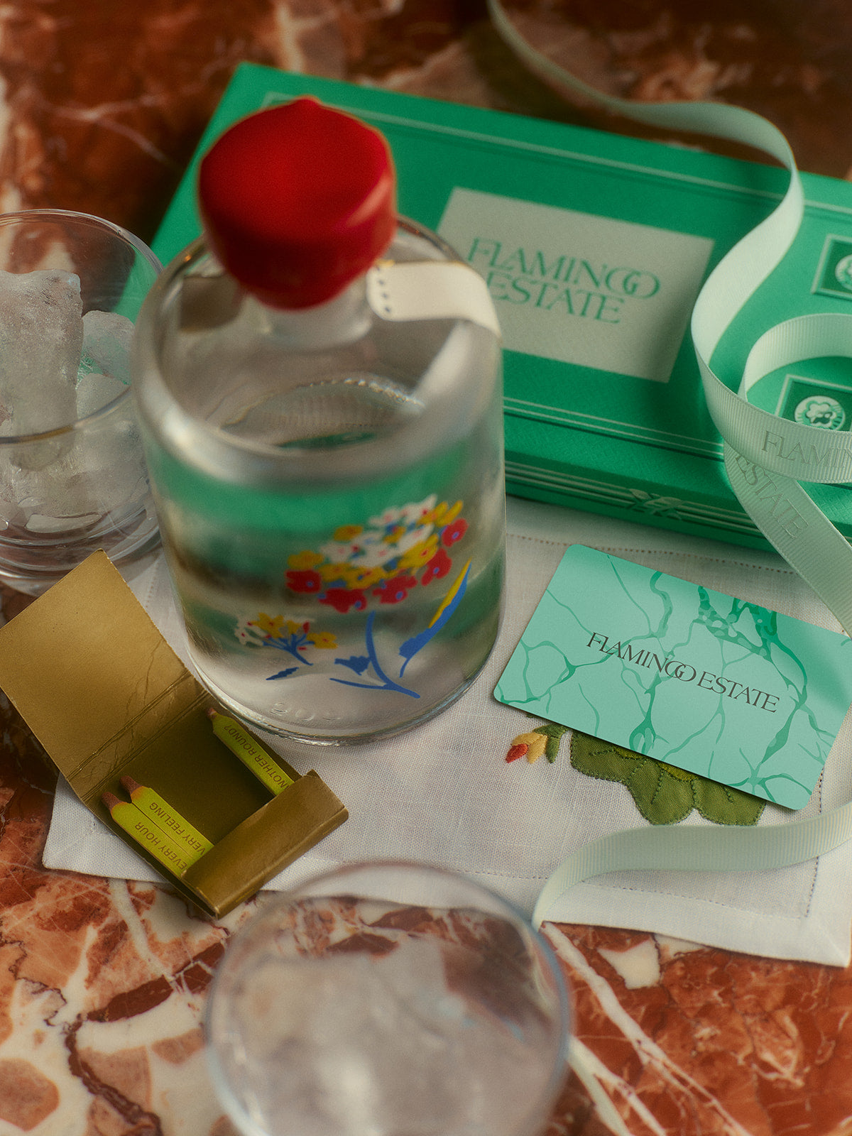A glass bottle with floral designs sits on a marble surface beside a Flamingo Estate card.