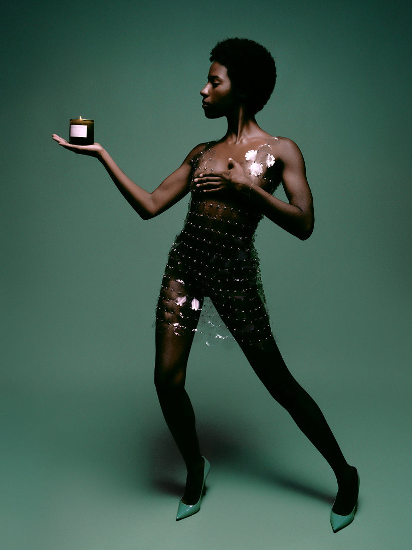 Woman in a sparkling outfit holding a small object Green Goddess candle with green background