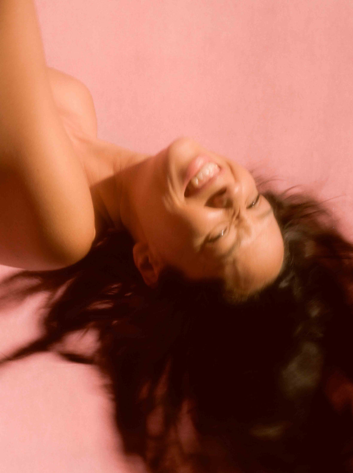 A person is lying down, smiling broadly with long hair spread out.