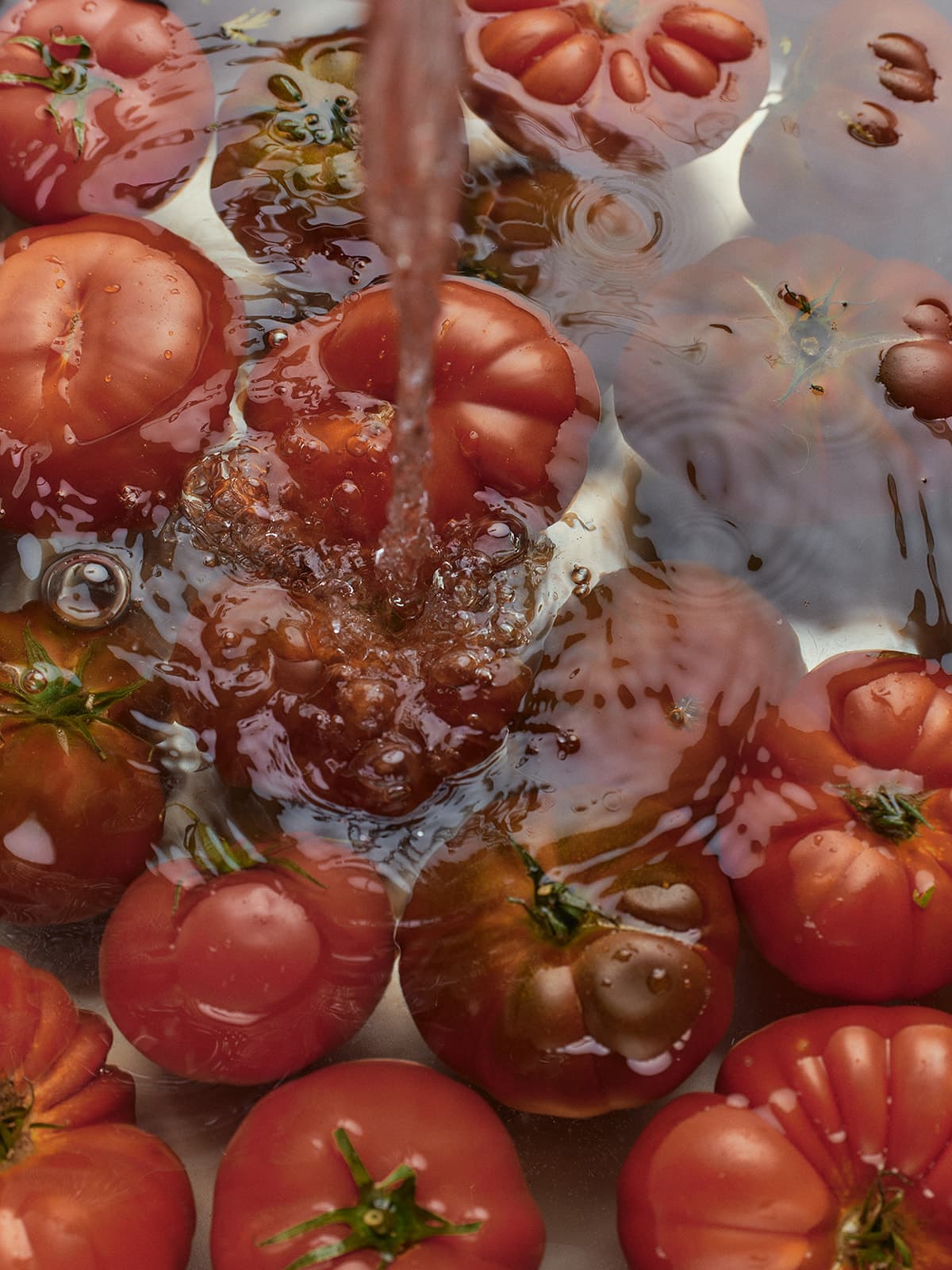 Tomatoes being washed under running water, creating bubbles and ripples.