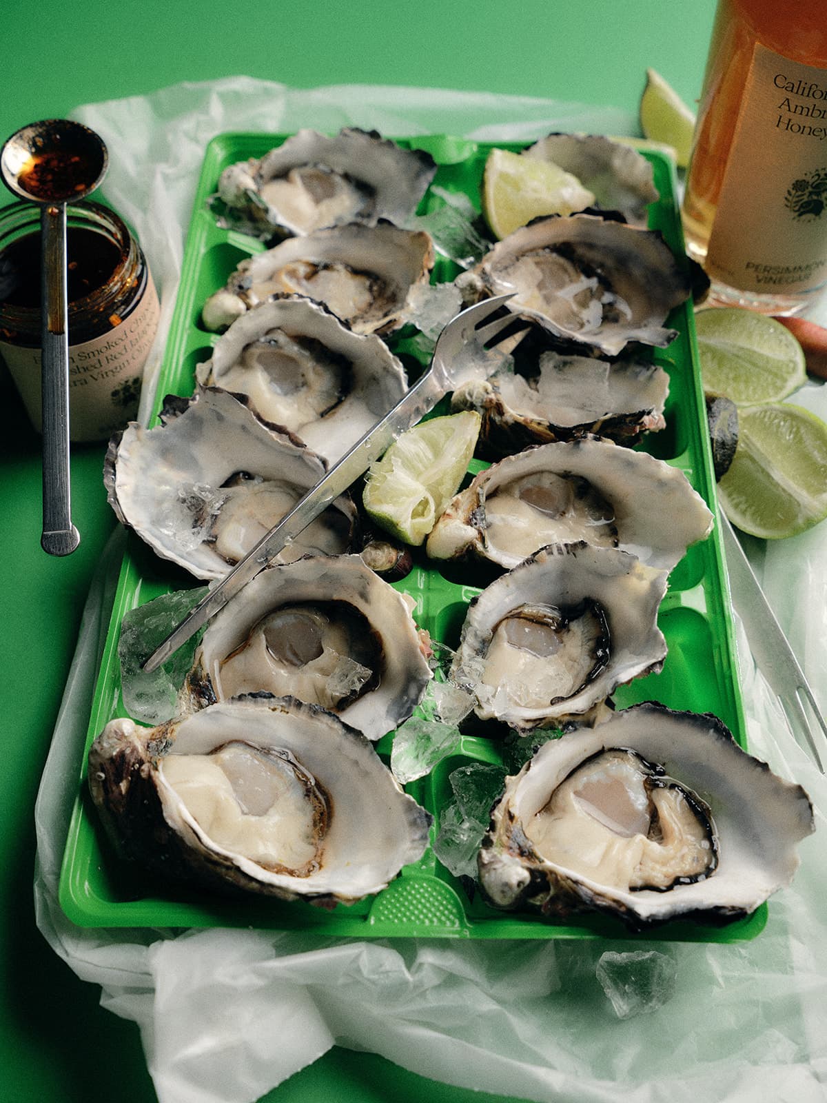 A green tray holds a dozen opened oysters on ice.
