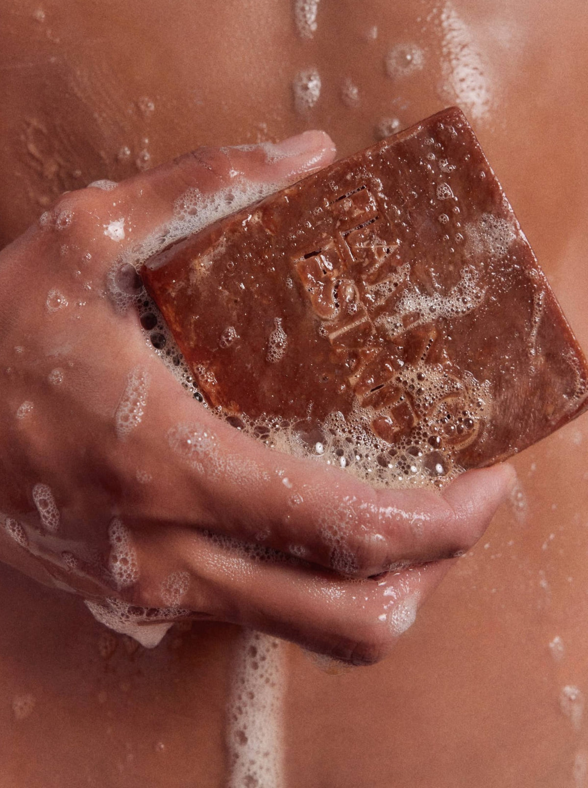 A person holds a rectangular bar of soap under running water.