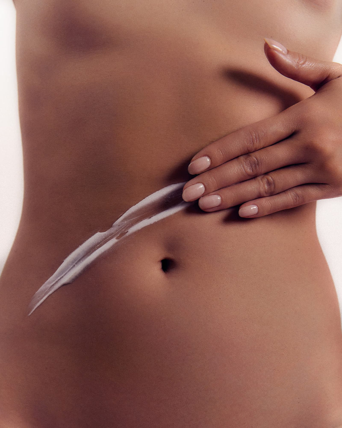 A hand gently applies a streak of white cream on a bare torso.