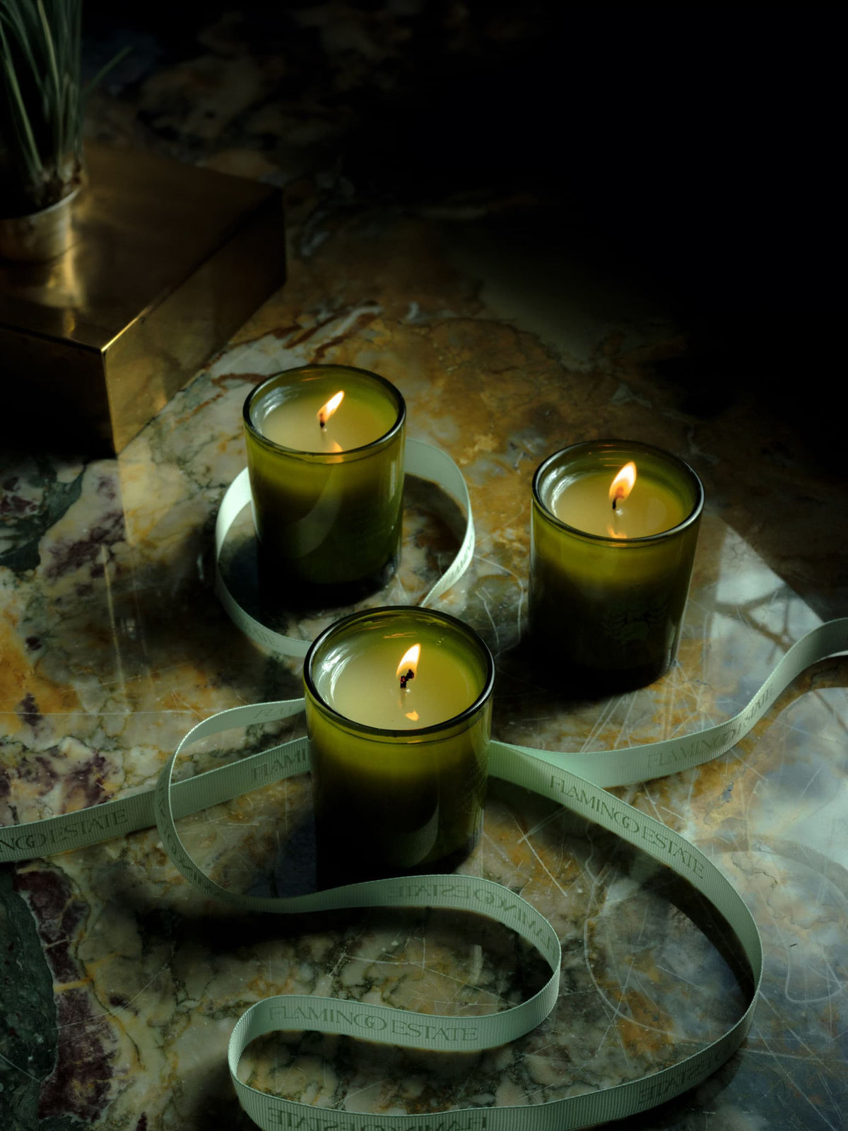 Three lit green candles stand on a marble surface, surrounded by a light green ribbon.