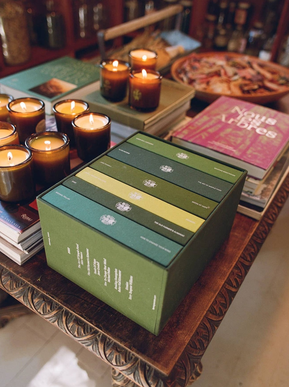 Candles flicker on a wooden table surrounded by books.