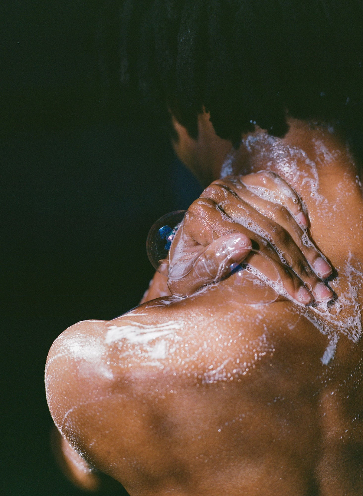 Person rinsing hair under water, with hands holding the head.