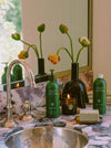 Flamingo Estate Products On A Marble Sink Unit In Front Of A Vase With Three Flowers
