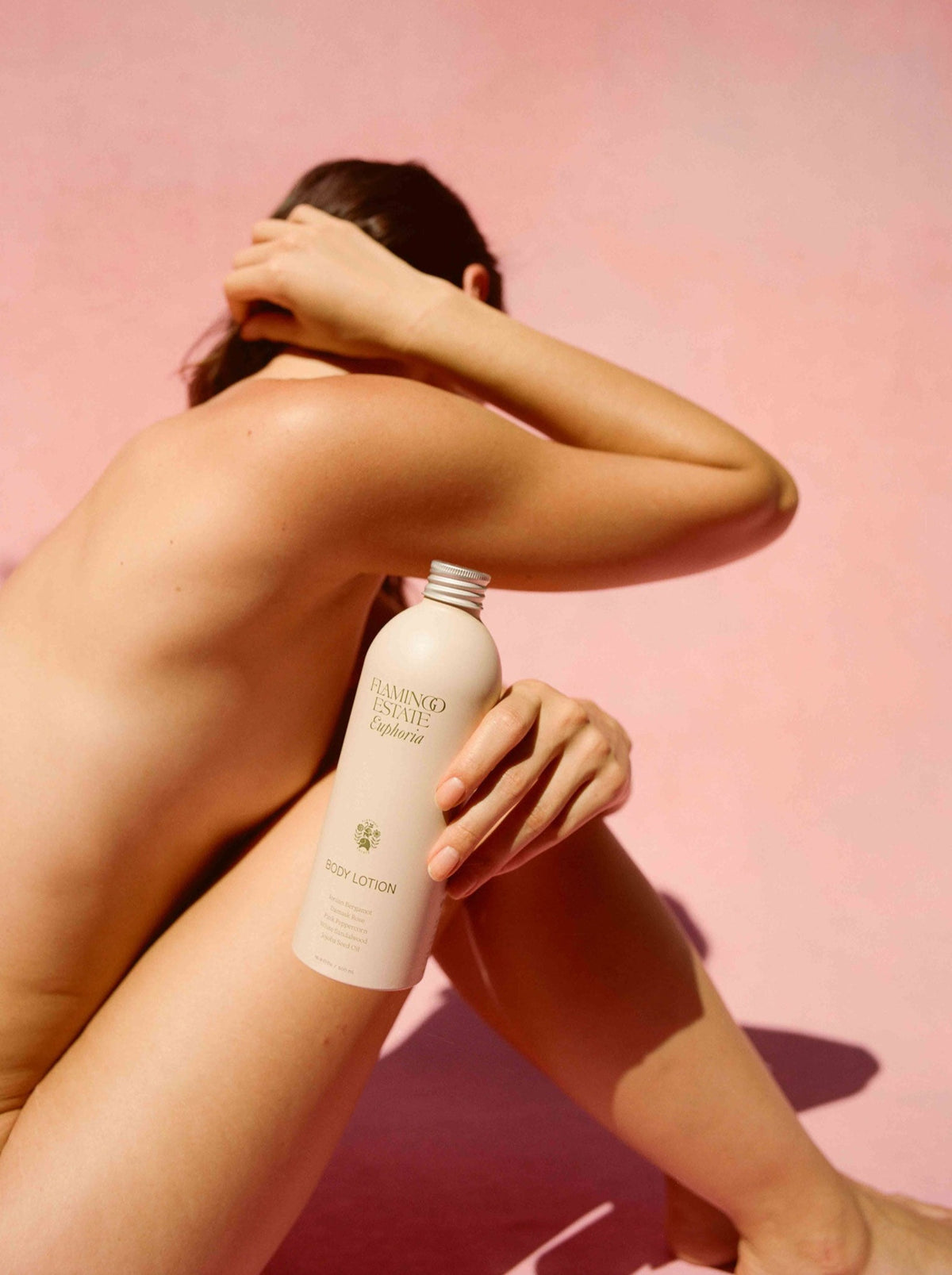 A person sits against a pink background, holding a bottle labeled 