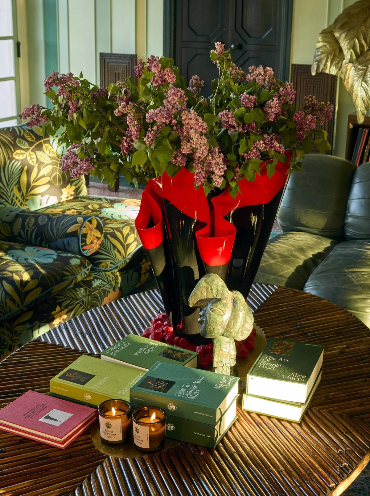 A large vase of pink flowers sits on a table, surrounded by books and candles.