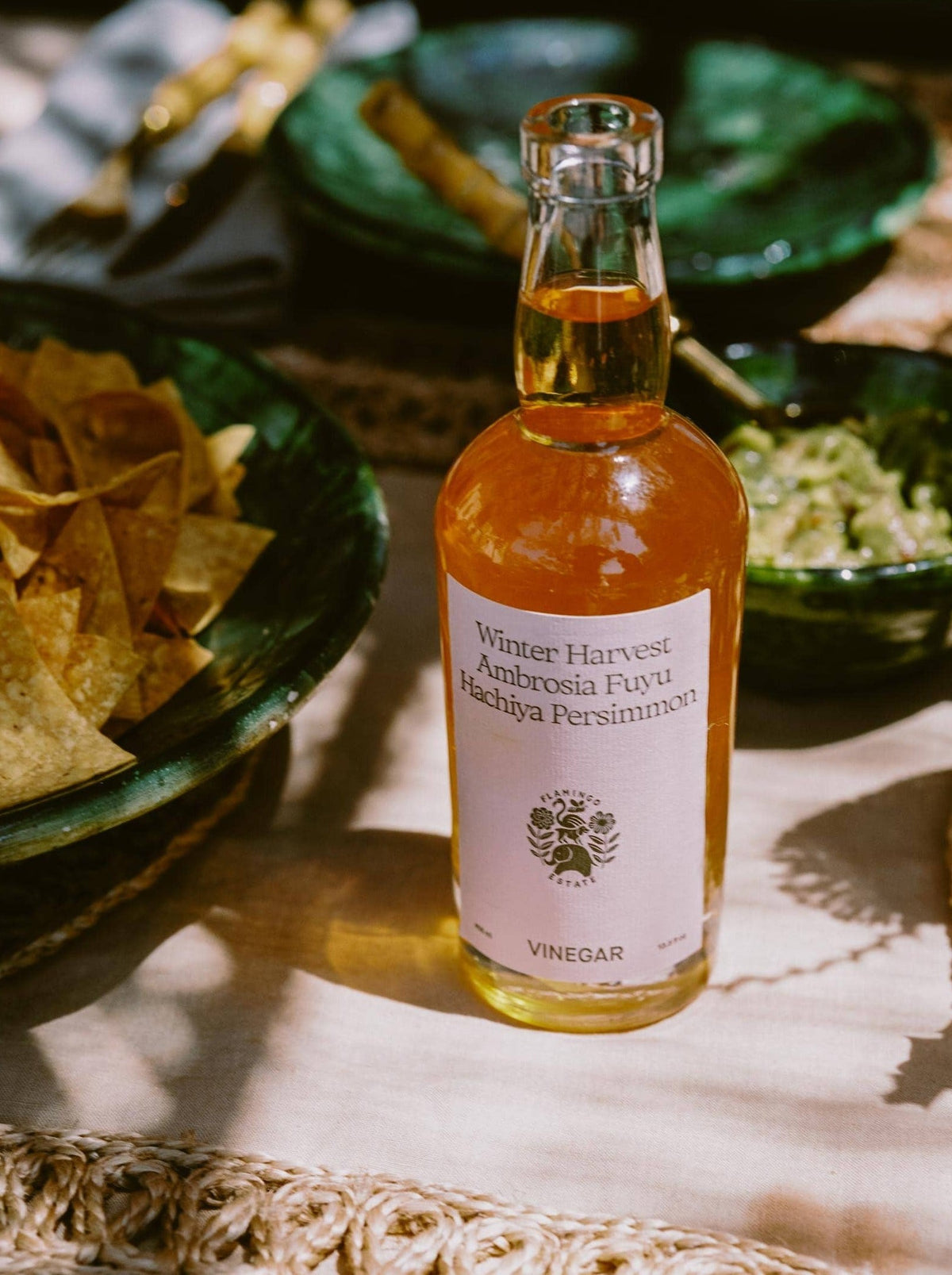 A beverage bottle stands on a sunlit table surrounded by green bowls.